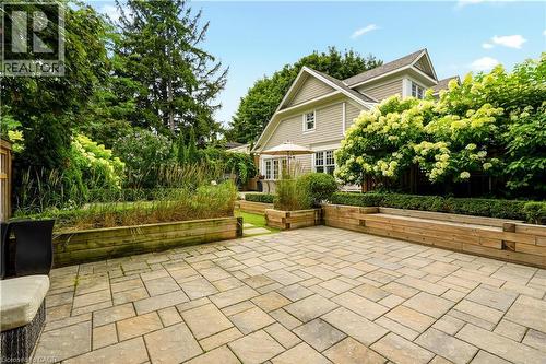 Expansive paver patio bordered by wooden raised garden beds, mature trees, and shrubs - 330 Camelot Court, Burlington, ON - Outdoor