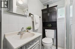 Bathroom featuring a white tile wainscoting, integrated vanity sink, decorative vanity cabinetry, dark wood-finish storage cabinet, and a glass-enclosed shower - 