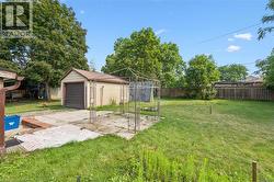 Expansive backyard featuring a detached garage, concrete patio, metal gazebo frame, and mature trees - 