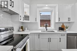 Modern kitchen featuring white shaker cabinetry with black hardware, white subway tile backsplash, stainless steel appliances, and a stainless steel sink with a matte black faucet - 