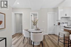 Open-concept dining area featuring wood-finish flooring, a contemporary white dining table, and recessed ceiling lighting - 