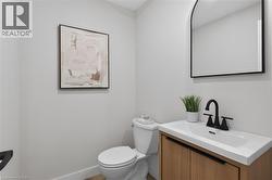 Modern powder room featuring a wood-finish vanity with an integrated white sink, matte black faucet, and an arched wall mirror - 