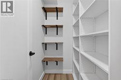 Dedicated storage area featuring white built-in shelving, wood-finish floating shelves with matte black brackets, a white door with matte black hardware, and wood-finish flooring - 
