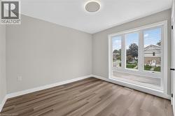 Bright room featuring a large, multi-pane window with white trim, wood-finish flooring, light gray walls, and white baseboards - 