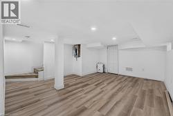Finished lower level featuring wood-finish flooring, recessed lighting, white walls, a utility door, and staircase access - 