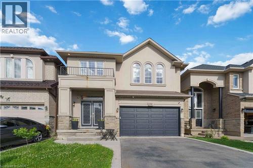 Contemporary stucco and stone exterior featuring an integrated garage, covered front entry, twin decorative double doors, and a second-story balcony with metal railing - 212 Chartwell Circle, Hamilton, ON - Outdoor With Facade