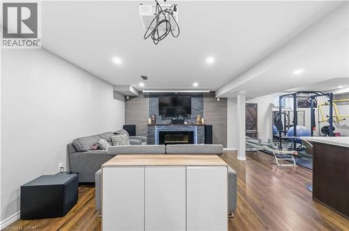 Finished basement featuring wood-finish flooring, recessed lighting, and a modern fireplace with a stone-accented wall - 212 Chartwell Circle, Hamilton, ON - Indoor With Fireplace