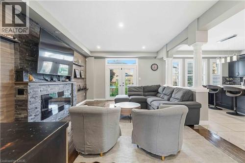Open-concept living area featuring a stone accent wall with built-in fireplace, wood-finish flooring, and white plantation shutters - 212 Chartwell Circle, Hamilton, ON - Indoor Photo Showing Living Room With Fireplace