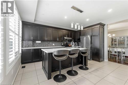 Kitchen featuring dark wood cabinetry, stainless steel appliances, a center island with countertop seating, and a mosaic tile backsplash - 212 Chartwell Circle, Hamilton, ON - Indoor Photo Showing Kitchen With Upgraded Kitchen