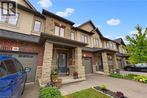 Contemporary townhome facade featuring brick and stone masonry, single-car garage with a panel door, covered front entry, and multiple windows with dark trim - 324 Equestrian Way Unit# 49, Cambridge, ON - Outdoor