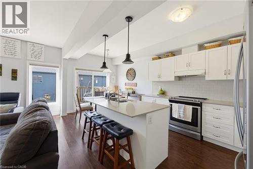 Open-concept kitchen featuring an island with pendant lighting, white cabinetry, integrated stainless steel appliances, light-toned countertops, and wood-finish flooring - 324 Equestrian Way Unit# 49, Cambridge, ON - Indoor Photo Showing Kitchen With Upgraded Kitchen