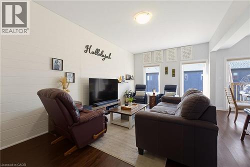 Living area featuring wood-finish flooring, white shiplap accent wall, recessed ceiling light, and multiple windows with roller shades - 324 Equestrian Way Unit# 49, Cambridge, ON - Indoor Photo Showing Living Room
