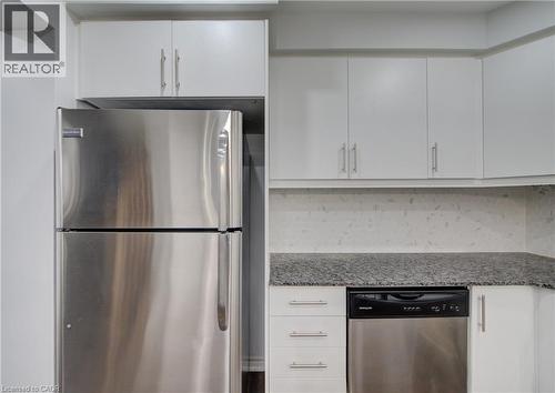Kitchen featuring stainless steel refrigerator, built-in stainless steel dishwasher, white cabinetry with brushed nickel hardware, light-toned backsplash, and dark granite countertops - 911 Apple Hill Lane, Kitchener, ON - Indoor Photo Showing Kitchen With Stainless Steel Kitchen