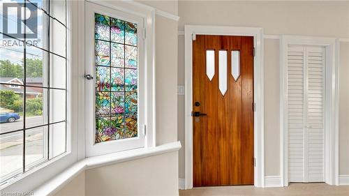 Hardwood entry door with decorative glass inserts, accompanied by a bay window featuring a stained-glass panel and grid-patterned panes - 59 Longwood Road N, Hamilton, ON - Indoor Photo Showing Other Room