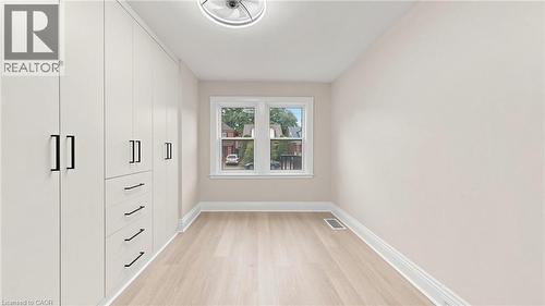Spacious room featuring a wall of integrated cabinetry with matte black hardware, light wood-finish flooring, and a contemporary ceiling light fixture - 59 Longwood Road N, Hamilton, ON - Indoor Photo Showing Other Room