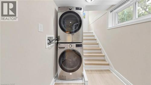 Dedicated laundry area featuring a stacked washer and dryer, light wood-finish flooring, and a window providing natural illumination - 59 Longwood Road N, Hamilton, ON - Indoor Photo Showing Laundry Room