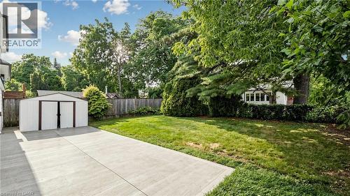 Expansive concrete patio with a detached storage shed, offering a manicured lawn and mature trees - 59 Longwood Road N, Hamilton, ON - Outdoor