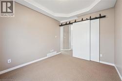 Room featuring tray ceiling, light neutral wall paint, patterned carpeting, white baseboards, and dual sliding barn doors with black hardware - 