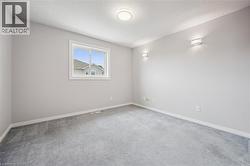 Carpeted room featuring a white-trimmed window, neutral wall paint, two wall-mounted sconces, a ceiling light fixture, and white baseboards - 