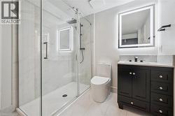 Modern bathroom featuring a glass-enclosed shower with tiled walls, a black vanity with a white countertop and rectangular sink, a lit mirror, a contemporary toilet, and tiled flooring - 