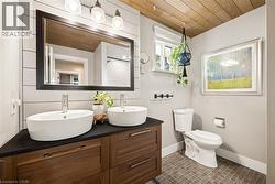 Bathroom featuring a wood-finish plank ceiling, a dual vanity with vessel sinks, and a dark countertop - 