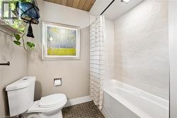 Bathroom featuring a white toilet, brown square tile flooring, light-toned wall tile in the shower, and a sloped wood-finish ceiling - 