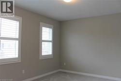 Neutral-toned room featuring two windows with white plantation shutters, light gray wall paint, white baseboards, and wall-to-wall carpeting - 