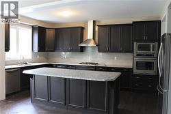 Modern kitchen featuring dark wood-finish cabinetry, light-toned countertops, a full suite of stainless steel appliances, a tiled backsplash, and recessed lighting - 