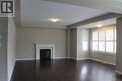Spacious room featuring dark wood-finish flooring, a white mantel fireplace, and multiple windows with plantation shutters - 