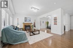 Open-concept living space featuring wood-finish flooring, a fireplace with a wood mantle and dark stone surround, and white plantation shutters - 