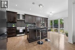 Gourmet kitchen featuring dark wood cabinetry, stainless steel appliances, a tile backsplash, and a central island with bar seating - 