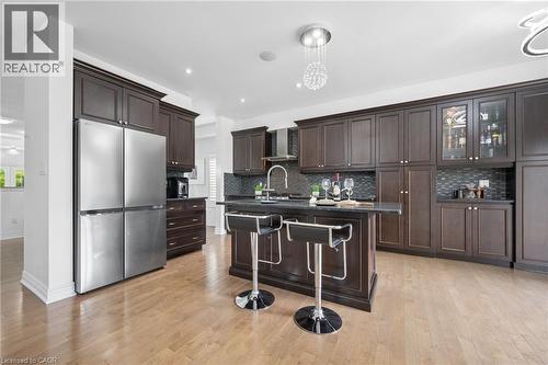 Kitchen featuring dark wood cabinetry, stainless steel appliances, a dark countertop island, a mosaic tile backsplash, and light wood-finish flooring - 145 Redtail Street, Kitchener, ON - Indoor Photo Showing Kitchen With Stainless Steel Kitchen With Upgraded Kitchen