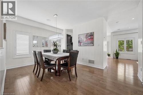 Dining area with wood-finish flooring, white plantation shutters, and a contemporary linear crystal chandelier - 145 Redtail Street, Kitchener, ON - Indoor Photo Showing Dining Room