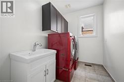 Laundry area featuring a single window, overhead cabinetry, a vanity with an integrated sink, and tiled flooring - 