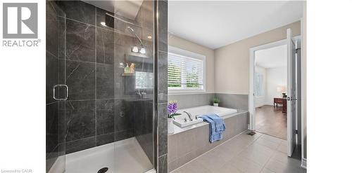 Spacious bathroom featuring a glass-enclosed shower with dark-toned tile surround, a built-in tub with light gray tile surround, and light tile flooring - 145 Redtail Street, Kitchener, ON - Indoor Photo Showing Bathroom