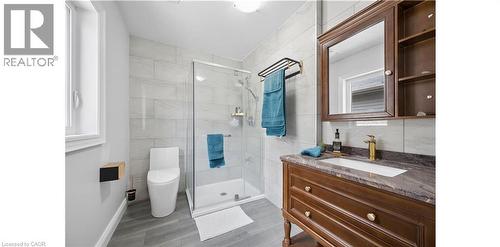 Contemporary bathroom featuring a glass-enclosed shower with tile surround, a modern toilet, wood-finish vanity with a stone countertop, an undermount sink, and a gold-finish faucet - 145 Redtail Street, Kitchener, ON - Indoor Photo Showing Bathroom