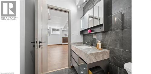 Bathroom featuring a built-in vanity with a stone countertop and integrated sink, a wall-mounted mirrored medicine cabinet, and large-format dark stone-look wall tiles - 145 Redtail Street, Kitchener, ON - Indoor Photo Showing Bathroom