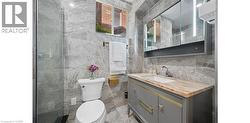 Bathroom featuring full-height marble-look tiling, a glass-enclosed shower, a vanity with a light-toned stone countertop, and an illuminated medicine cabinet - 