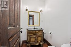 Powder room featuring a detailed wood-finish vanity with a dark countertop and integrated sink - 