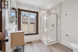 Contemporary bathroom featuring a glass-enclosed shower with white marble-look tile surround, a light wood-finish vanity, a wall-mounted mirror, and wood-finish flooring - 