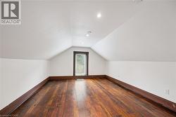 Attic space featuring wood-finish flooring, white walls, and a gabled ceiling with recessed lighting - 
