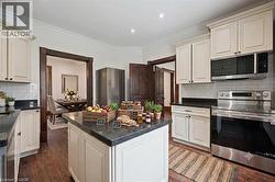 Kitchen featuring a central island with dark stone countertops, white cabinetry, a subway tile backsplash, stainless steel appliances, and wood-finish flooring - 