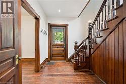 Foyer featuring wood-finish flooring, a traditional wood staircase with balusters, wood paneling, a wood entry door with glass upper portion, and wood trim - 