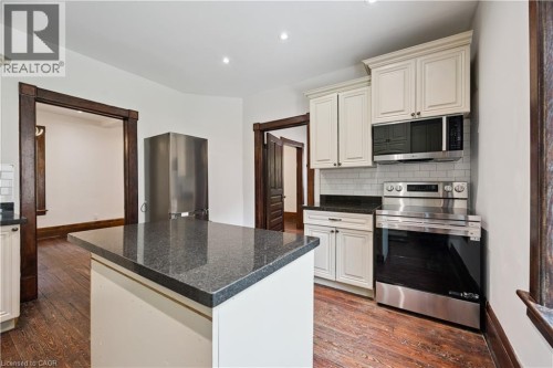 Kitchen featuring a central island with a dark stone countertop, white shaker-style cabinetry, subway tile backsplash, stainless steel range, and wood-finish flooring - 245 Lowther Street S, Cambridge, ON - Indoor Photo Showing Kitchen