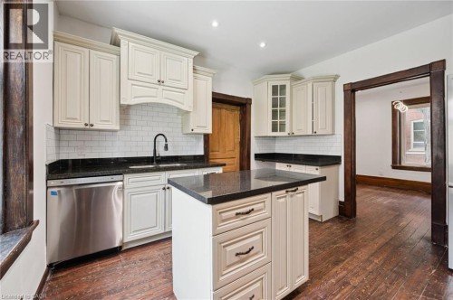 Kitchen featuring a central island with a dark countertop, white cabinetry with dark hardware, a stainless steel dishwasher, a white subway tile backsplash, and dark wood-finish flooring - 245 Lowther Street S, Cambridge, ON - Indoor Photo Showing Kitchen With Upgraded Kitchen