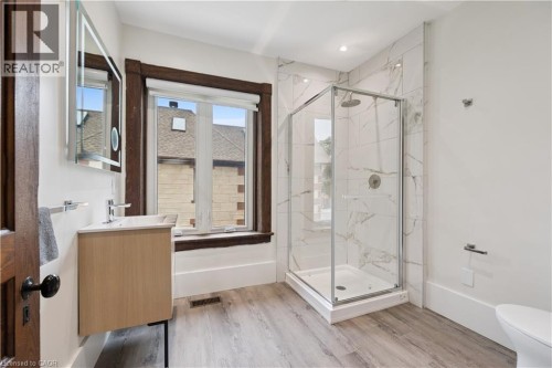 Contemporary bathroom featuring a glass-enclosed shower with white marble-look tile surround, a light wood-finish vanity, a wall-mounted mirror, and wood-finish flooring - 245 Lowther Street S, Cambridge, ON - Indoor Photo Showing Bathroom