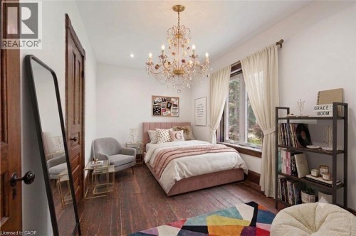 Spacious room featuring hardwood flooring, a large window, a decorative chandelier, and a solid wood door - 245 Lowther Street S, Cambridge, ON - Indoor Photo Showing Bedroom