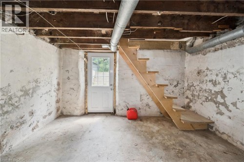 Unfinished basement space featuring exposed wood joists, concrete flooring, and a white paneled door with windowpanes - 245 Lowther Street S, Cambridge, ON - Indoor Photo Showing Basement