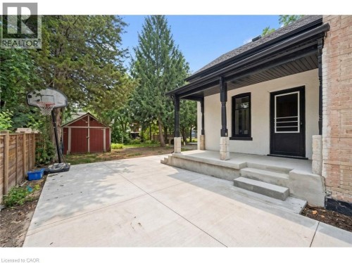 Concrete patio area featuring a covered porch with black columns, a brick exterior wall, and a red garden shed - 245 Lowther Street S, Cambridge, ON - Outdoor With Deck Patio Veranda