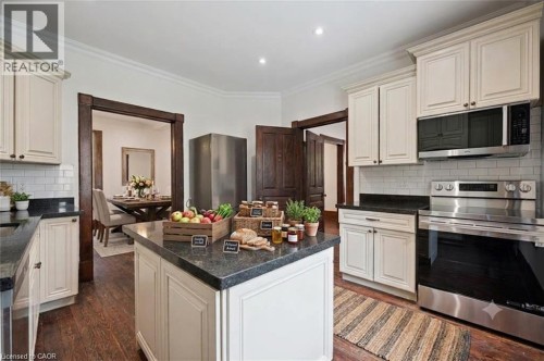 Kitchen featuring a central island with dark stone countertops, white cabinetry, a subway tile backsplash, stainless steel appliances, and wood-finish flooring - 245 Lowther Street S, Cambridge, ON - Indoor Photo Showing Kitchen